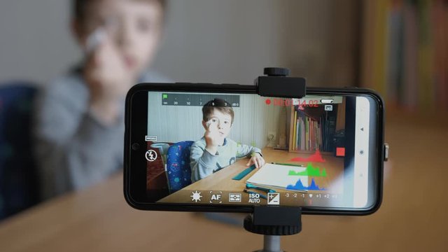 Schoolboy makes his first video blog. He draws a car with a pencil, ruler and drawing compass. Using his phone and mini tripod to shoot video.