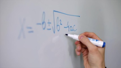 hand with marker pen on whiteboard creating a maths quadratic equation in close up.
