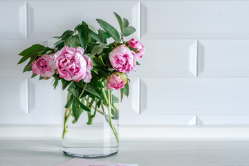 Bouquet of pink peonies in glass vase against white background and wooden table. Mothers day card. Beautiful peony flower for catalog or online store. Floral shop and delivery concept. Copy space.