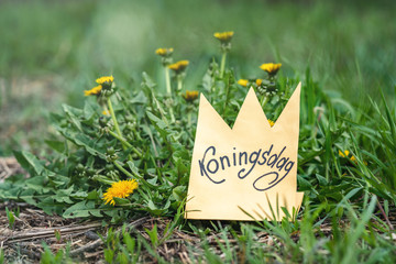 Koningsdag or King's Day is a national holiday in the Kingdom of the Netherlands. Paper cut crown with an inscription koningsdag on the dandelion field