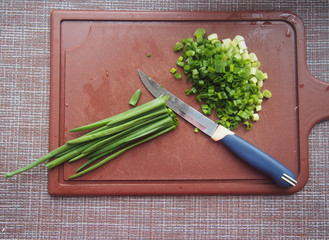 Onion leaves and a knife lie on a brown plastic chopping Board.