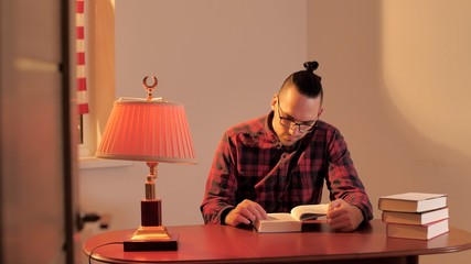 Guy or man sits at antique wooden table and reads a book. Early morning in quarantine due to...