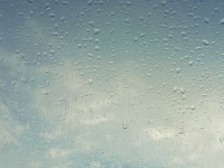 Wet window with rain drops and a cloudy sky outside.