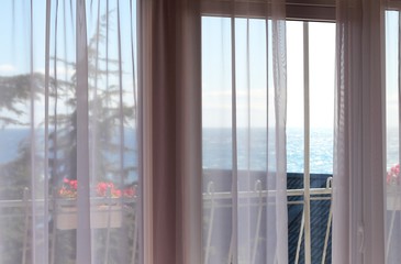 Window and white curtains with view of sea in hotel room.