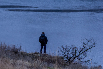 a man looks from a cliff to the water. Gloomy autumn landscape. A lone tree and a man on the edge.