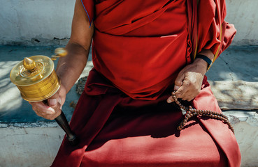Hands of a Tibetan Buddhist monk with a spinning Tibetan prayer wheel and wooden Mala, in Ladakh, North West India - obrazy, fototapety, plakaty