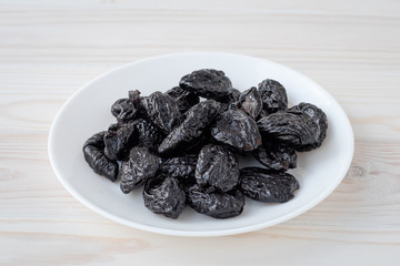A heap of prune on white plate on wooden boards background. Vegetarian food. Dry plum. Healthy eating concept.