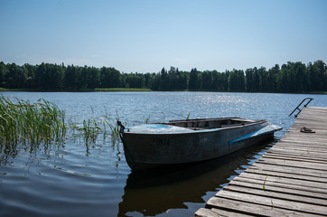 A boat in lake surrounded by green forest. Boat next to the wooden pier on a calm day.