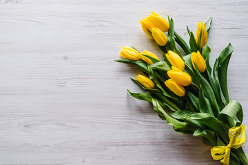 Bouquet of yellow tulips on white wooden background with space for message. Summer flowers concept. Spring. Holiday greeting card for Valentine's, Women's, Mother's Day, Easter. Top view, flat lay.