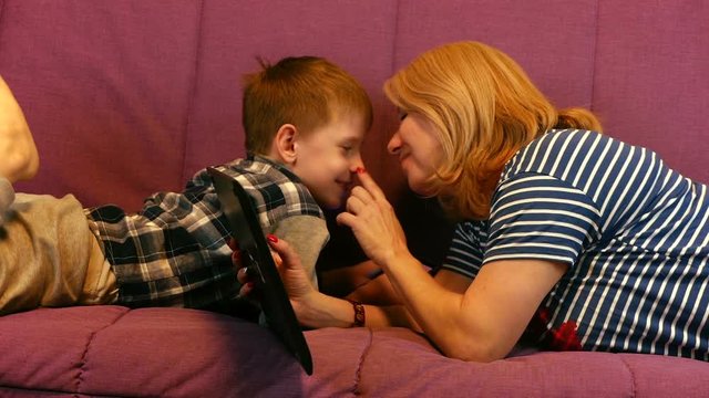 Happy mom with her son at home on the sofa lie with a phone and laptop. Quarantined Lifestyle