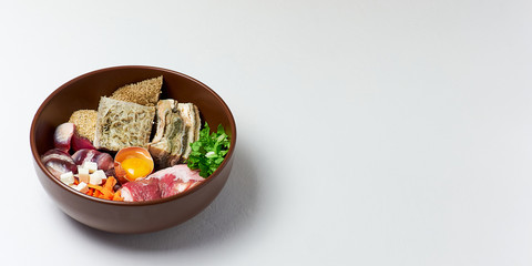 Natural organic dog food in big brown bowl over white background. Raw meat, beef tripe, poultry gizzard, egg, vegetables and food supplements. Copy space.