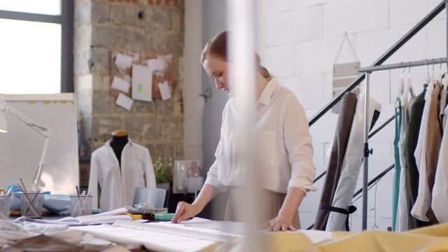 Professional female dressmaker working with fabric while making new garment in sewing studio