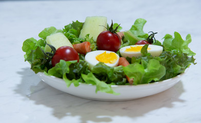 Tasty fresh mix vegetable salad on white dish  on white marble background