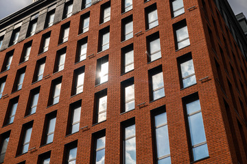 Fototapeta premium Red brick building wall fragment with clouds reflections in windows 