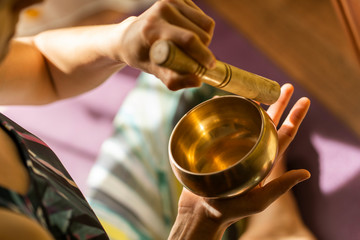 Fototapeta na wymiar Top view of a young yogin woman holding a tibetan bowl and a stick in the beautiful and gentle light of morning during a yoga session, creating a meditative state through music.