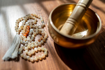 Handmade sacred mala seed beads and a golden Tibetan bowl on a wooden background in the soft and...