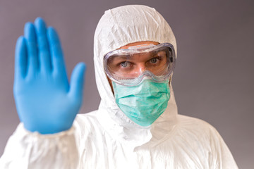Male doctor with surgical mask, goggles and protective suit showing stop on gray backround.