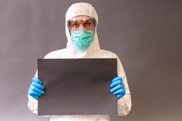Doctor with surgical mask, goggles and protective suit holding a black banner on gray backround.