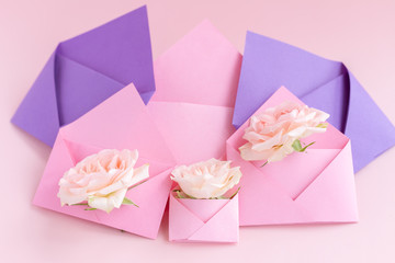 Purple and pink paper open envelopes with full small rose flowers on color background. Spring, summer concept. Romance, love notes, greeting card for March 8 International Woman's, Valentine's day