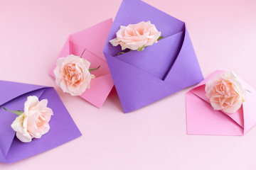 Fototapeta na wymiar Purple and pink paper open envelopes with full small rose flowers on color background. Spring, summer concept. Romance, love notes, greeting card for March 8 International Woman's, Valentine's day