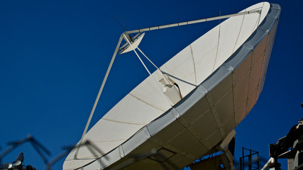 Large satellite dish. TV and radio broadcasting antenna. In front of blue sky.