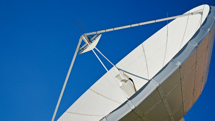 Large satellite dish. TV and radio broadcasting antenna. In front of blue sky.