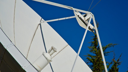 Large satellite dish. TV and radio broadcasting antenna. In front of blue sky.
