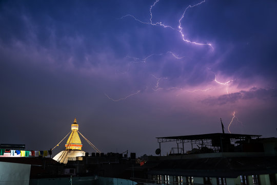 A thunderstorm front rages over the city of Kathmandu, in the place where Boudha Stupa is located. Lightning strikes, clouds and a stupa with night illumination are visible.