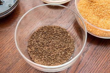 cumin seeds in a glass bowl on a wooden table next to other spices