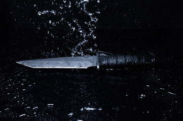 Splashes of water pour on the knife. A knife under the pressure of water. Water and a knife.