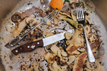 A metal sink in which there are two forks, a knife with a wooden handle and potato peel. The...