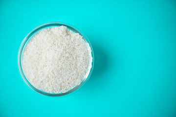 Rice bowl, uncooked rice, grains on sky blue background, isolated with copy space. White rice polish and cooked for daily meal. Vegetarian, vegan food widely used in Asian cuisine.