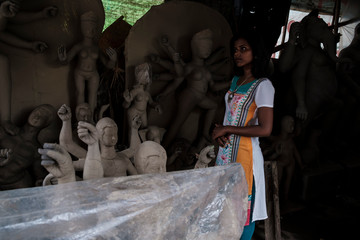Portrait of a beautiful brunette Indian lady in white ethnic dress standing in front of clay idols...