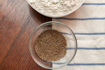 .caraway seeds in a glass bowl on a wooden table next to flour. homemade baking
