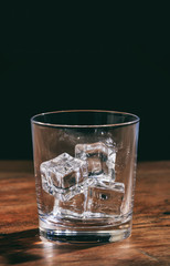 Crystal whiskey glass with ice cubes on a wooden table.
