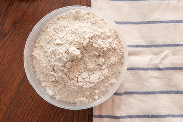 flour in a bowl on a wooden table and a towel. homemade baking