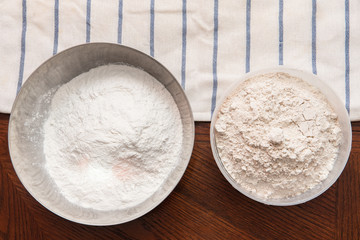 two bowls with flour on a wooden table and a towel. homemade baking