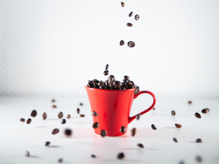 
Roasted coffee beans, dipping into a red coffee cup, on a white background