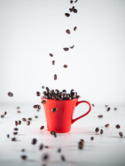 
Roasted coffee beans, dipping into a red coffee cup, on a white background
