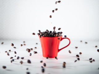 
Roasted coffee beans, dipping into a red coffee cup, on a white background