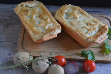Scottish pie on a wooden cutting board next to onions, tomatoes and a wooden spoon