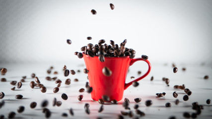 
Roasted coffee beans, dipping into a red coffee cup, on a white background