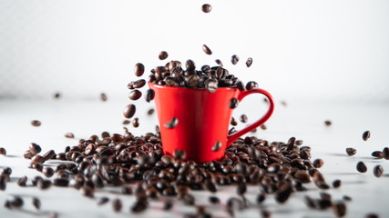 
Roasted coffee beans, dipping into a red coffee cup, on a white background