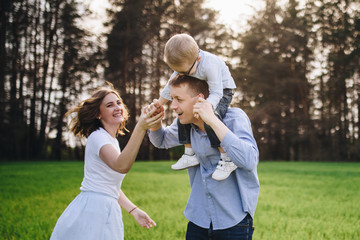 Obraz premium Family in nature. Picnic in the forest, in the meadow. Green grass. Blue clothes. Mom, dad, son with glasses. Boy with blond hair. Joy. Parents play with child. Together. Picnic basket. Food, blanket