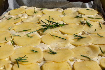 Raw Focaccia dough with potatoes and rosemary, before baking.