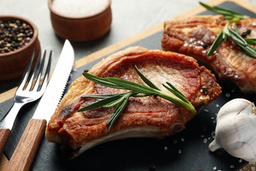 Board with steaks and cutlery on gray background. Grilled food