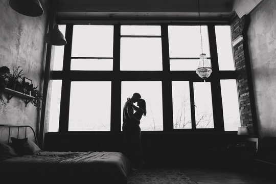 silhouette of young couple standing  and hugging against window background indoors. portrait of young beautiful couple. 