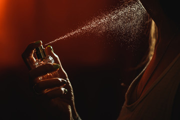 a girl on a dark background sprays perfume on her neck, every drop is visible