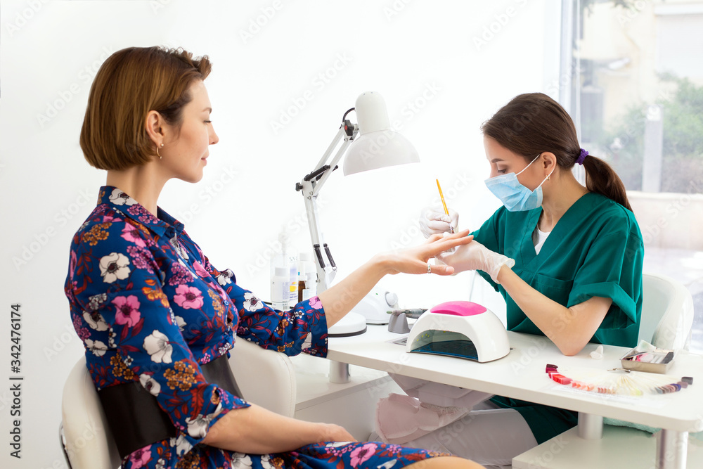 Wall mural Master manicurist prepares nails for applying gel polish on client's hands. The process of professional manicures. The concept of beauty and health. Beautiful female client looking at a manicurist.