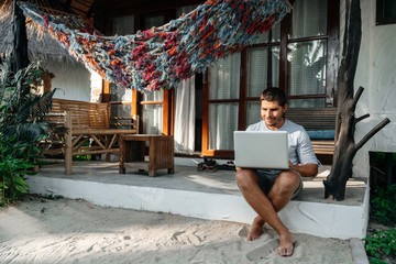 A man uses a laptop while sitting on the terrace of his house. Remote work on the Internet in...